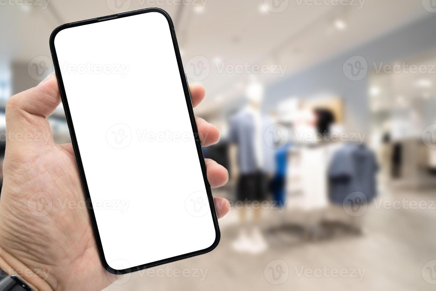 Hand holding blank screen smartphone for copy space on blurred clothing store. e-commerce app shopping mockup. social media, payment and shopping online concept. fashion and technology. photo