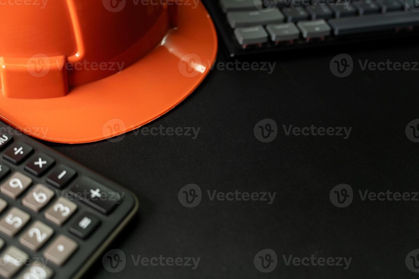 Orange safety helmet or hard hat, keyboard and calculator on black background. Business building idea or engineering context. Top view with copy space. photo