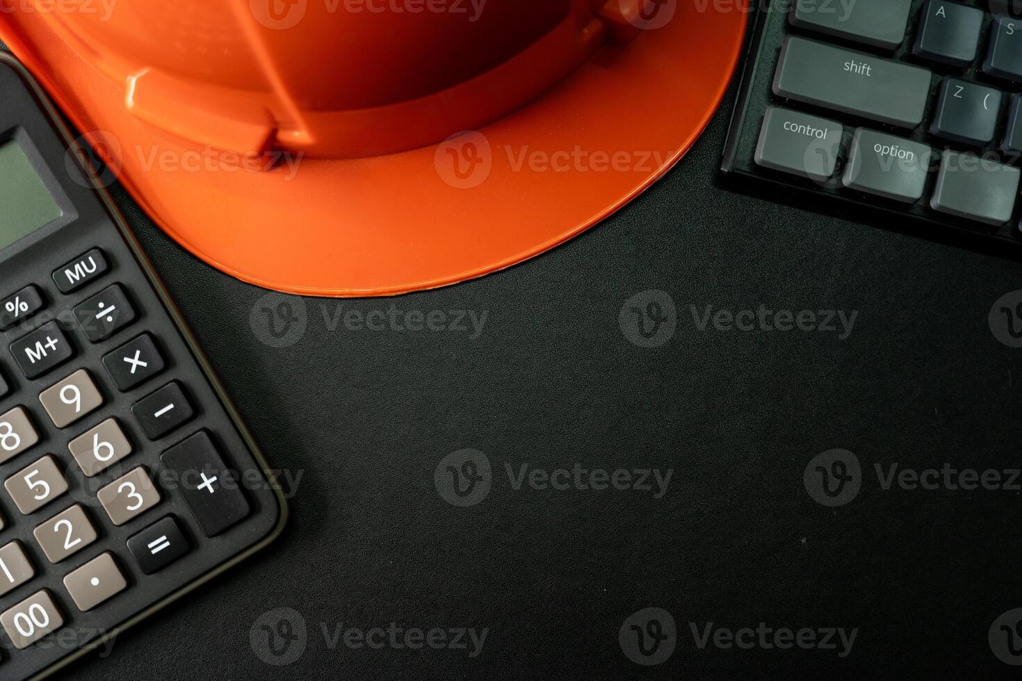 Orange safety helmet or hard hat, keyboard and calculator on black background. Business building idea or engineering context. Top view with copy space. photo