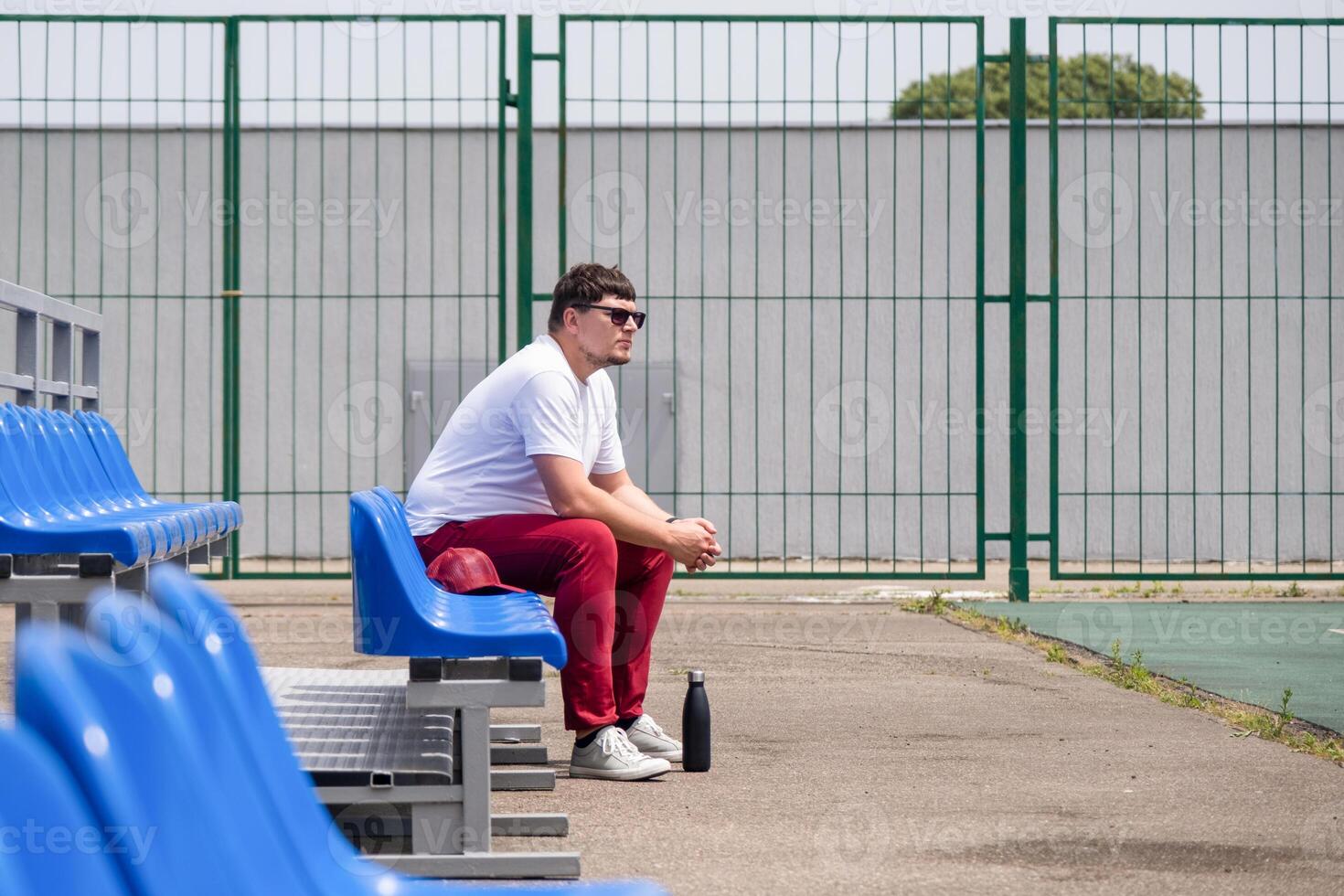 sportsman with a bottle of water sitting and resting at the seats at the stadium photo