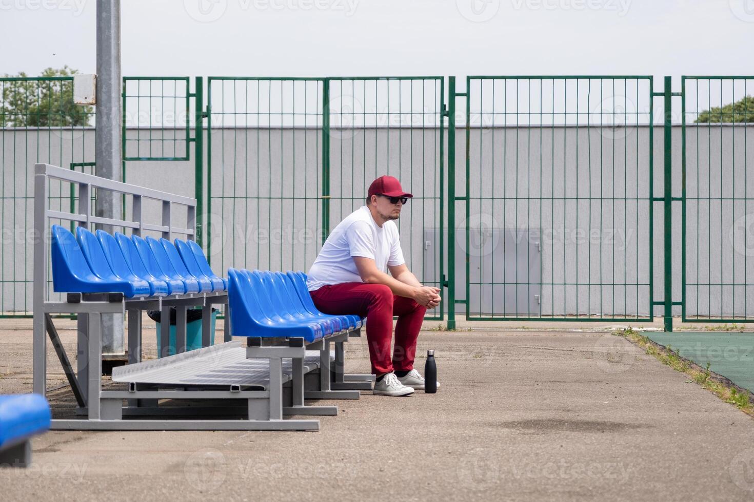 sportsman with a bottle of water sitting and resting at the seats at the stadium photo
