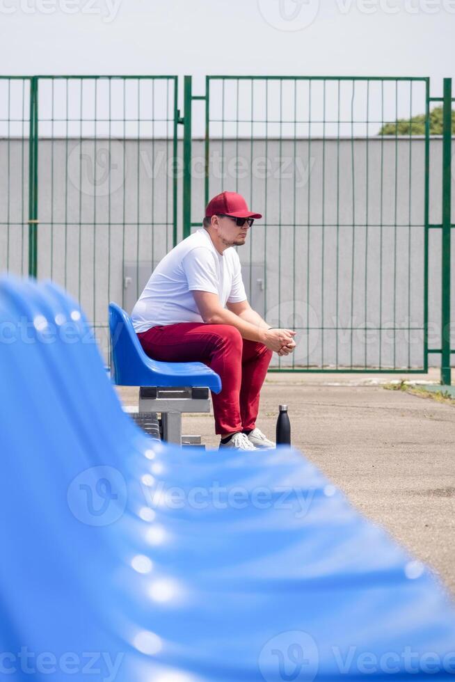 sportsman with a bottle of water sitting and resting at the seats at the stadium photo