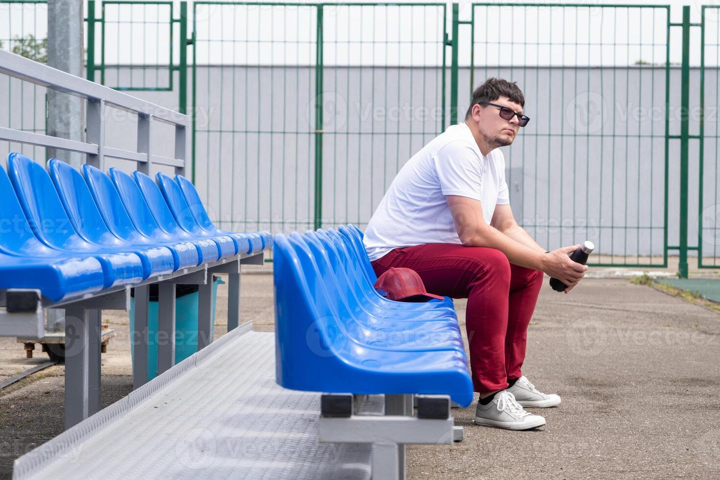 sportsman with a bottle of water sitting and resting at the seats at the stadium photo