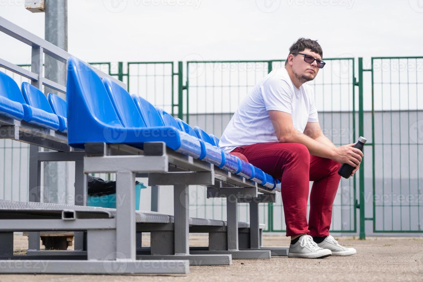 sportsman with a bottle of water sitting and resting at the seats at the stadium photo