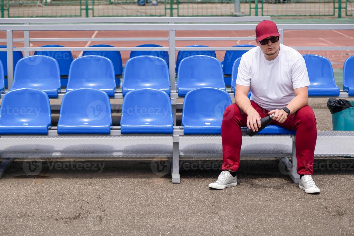 sportsman with a bottle of water sitting and resting at the seats at the stadium photo