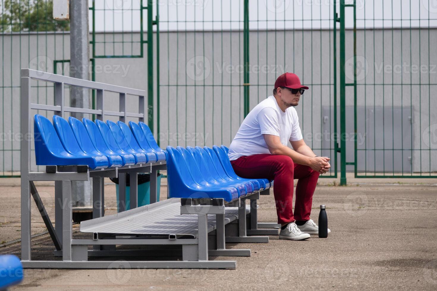 sportsman with a bottle of water sitting and resting at the seats at the stadium photo