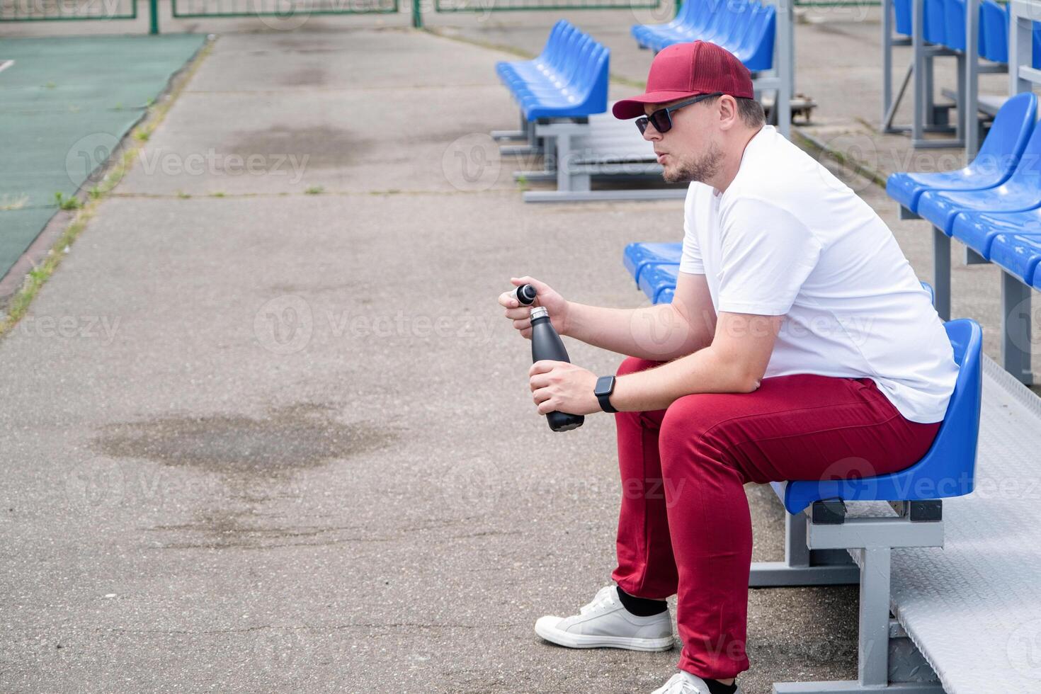sportsman with a bottle of water sitting and resting at the seats at the stadium photo