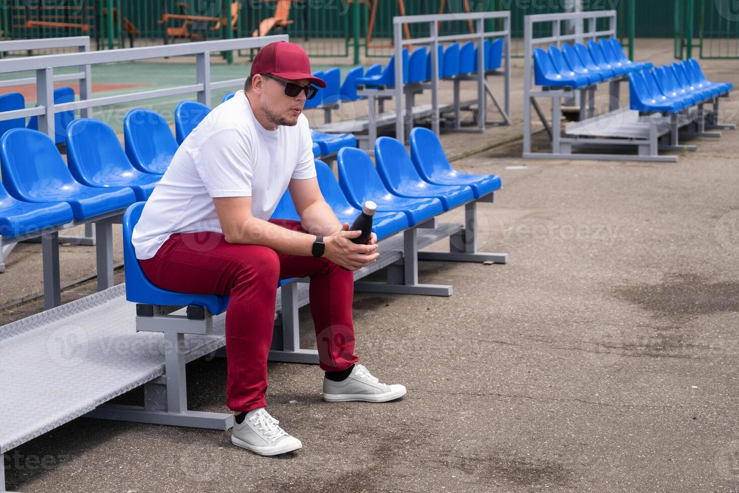 sportsman with a bottle of water sitting and resting at the seats at the stadium photo