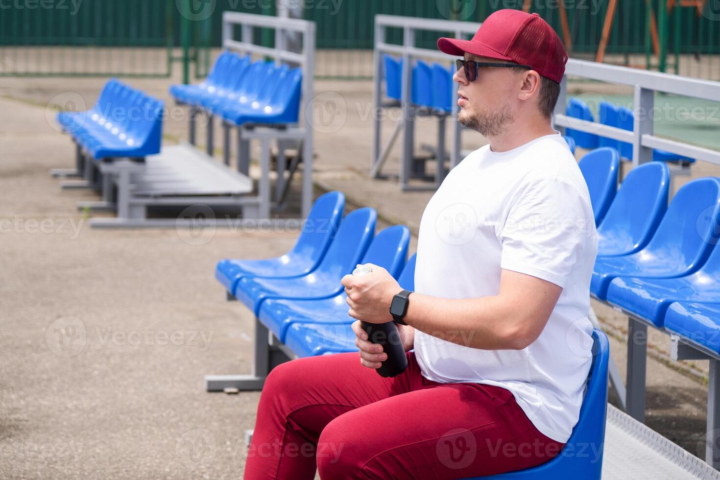 sportsman with a bottle of water sitting and resting at the seats at the stadium photo