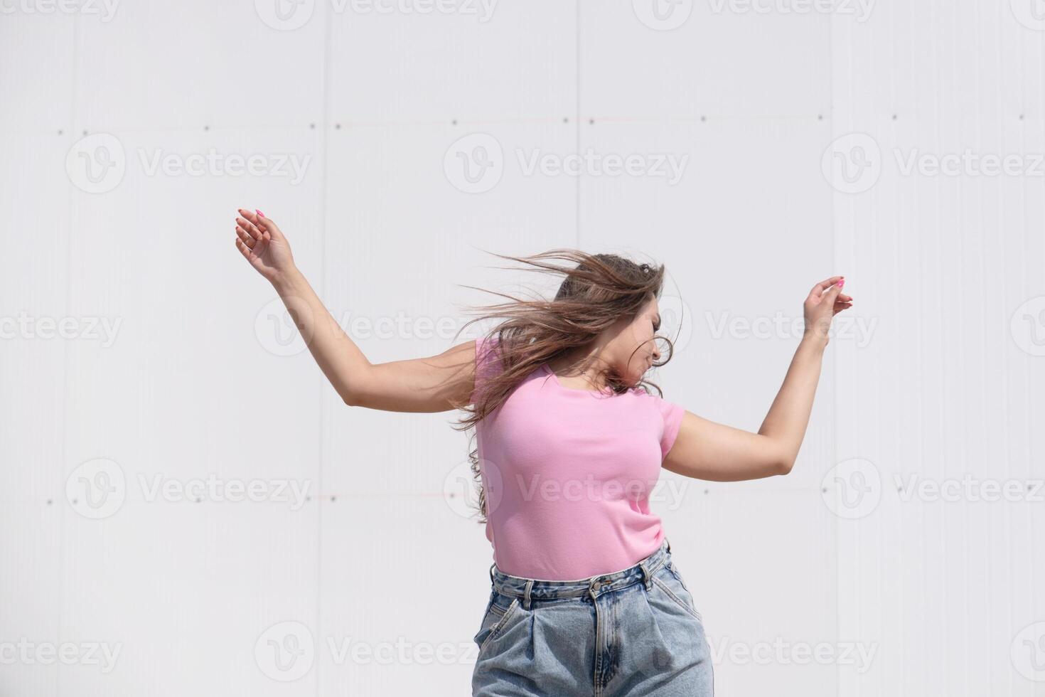 plus size woman wearing casual clothes dancing on white wall background in the street photo