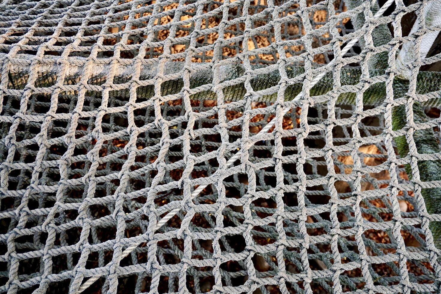 Thick rope with net pattern isolated on outdoor park playground horizontal ratio dry brown fallen leaves on ground background. photo