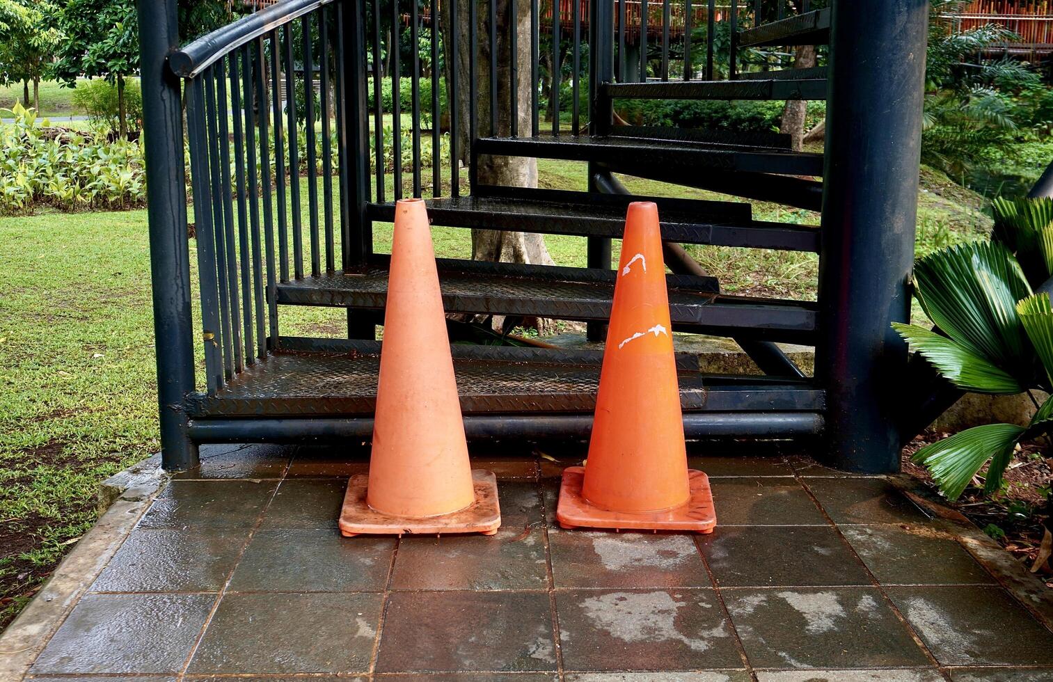 Two orange triangle traffic cone barrier as a do not climb or enter sign isolated on horizontal ratio outdoor park environment and black metal staircase objects. photo