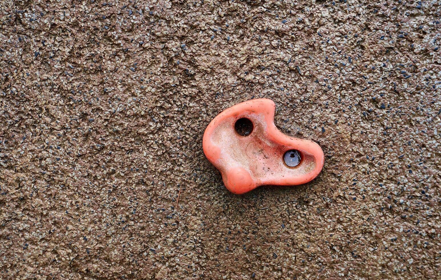 Orange or red colored outdoor children toy playground climbing wall rock activity isolated on horizontal ratio empty copy spaced stone wall texture background. photo
