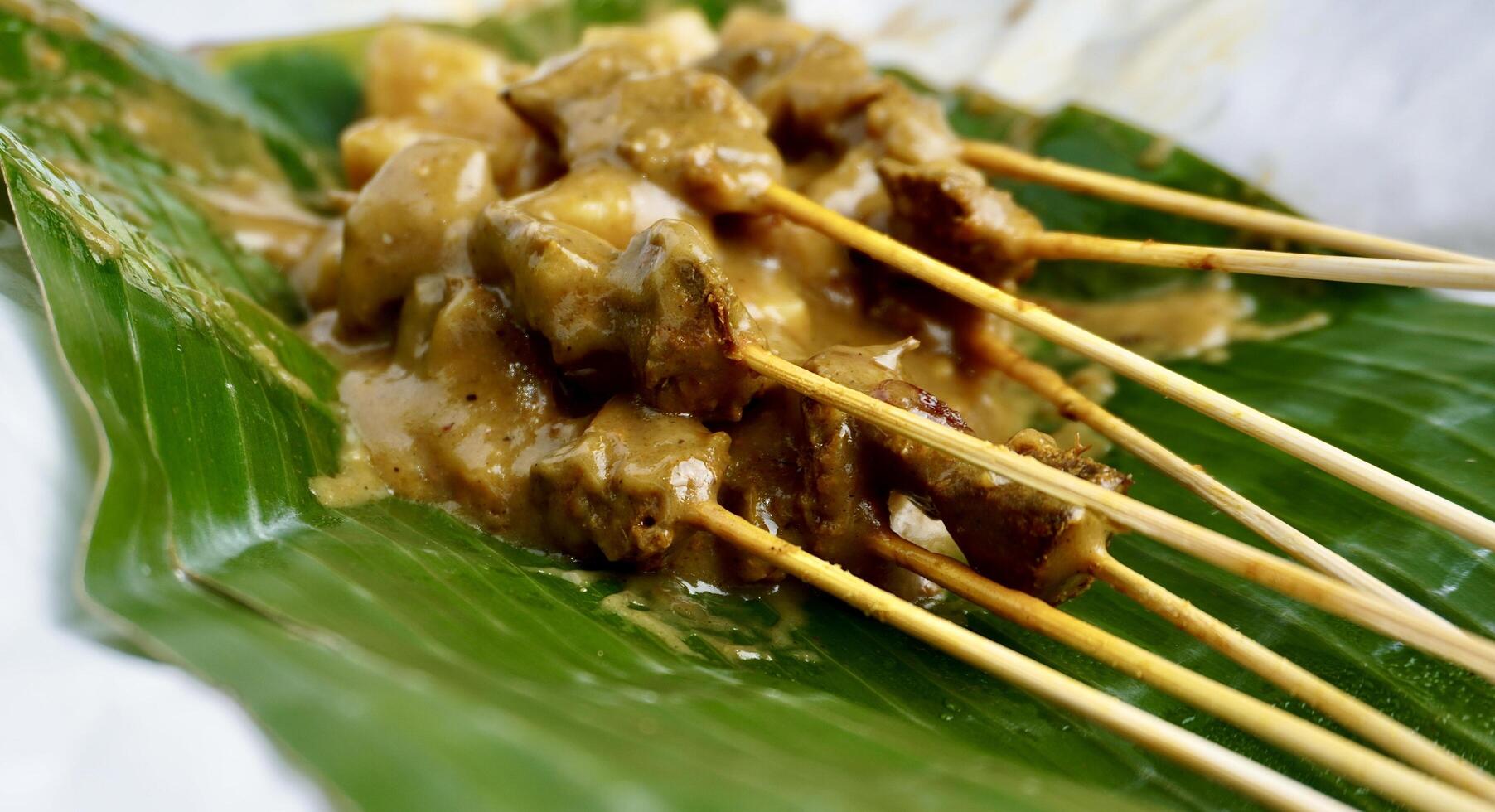 Delicious sate padang dish from Indonesia on top of paper plate and green banana leaf background. Beef skewers with sauces and ketupat rice cakes. photo