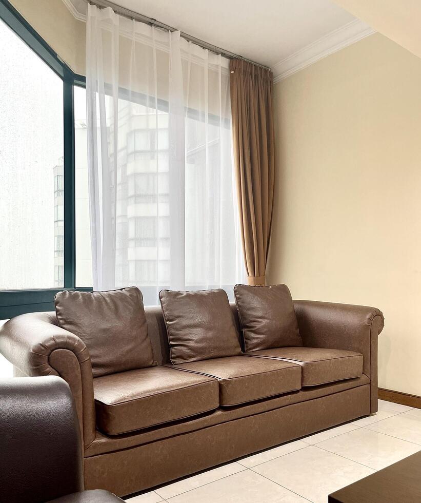 Indoor apartment environment with wide window with brown curtains, brown leather sofa chair, and light plain yellow walls isolated on vertical ratio background photography. photo