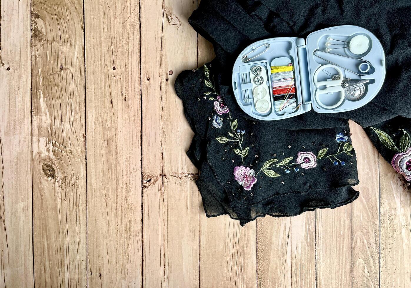 Travel size compact sewing tailoring kit on black flower clothing fabric. Object photography isolated on horizontal wooden table desk background with empty copy space for texts. photo