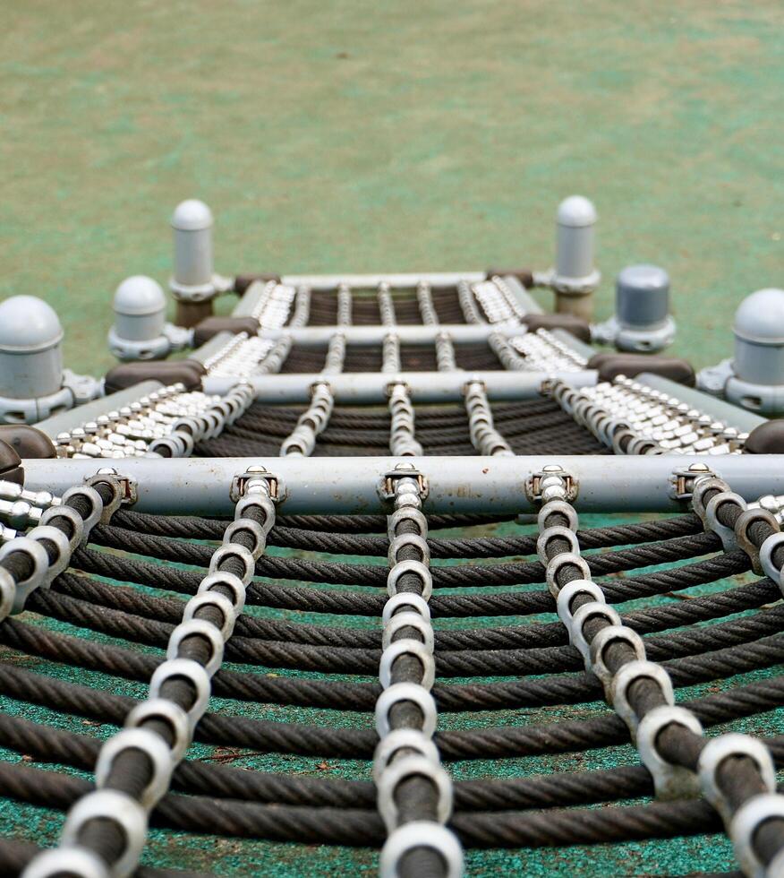 Black rope with net shapes tied on steel structure isolated on vertical ratio first person pov above angle view outdoor playground green flooring environment. photo