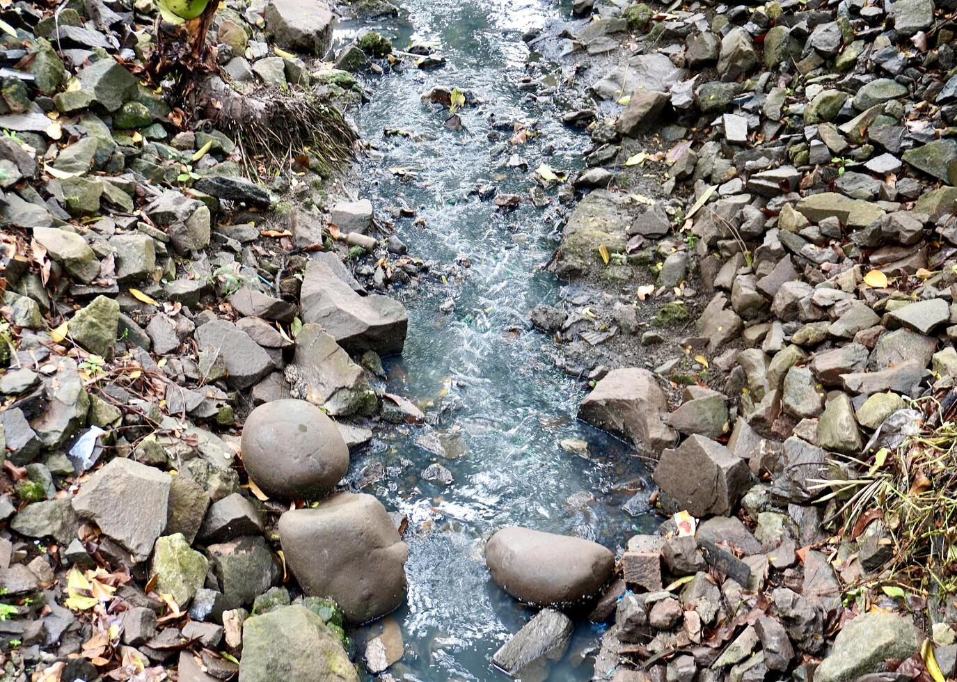 Narrow rough water stream flow between rock stones and pebbles isolated on horizontal ratio background on outdoor environment background photography. photo