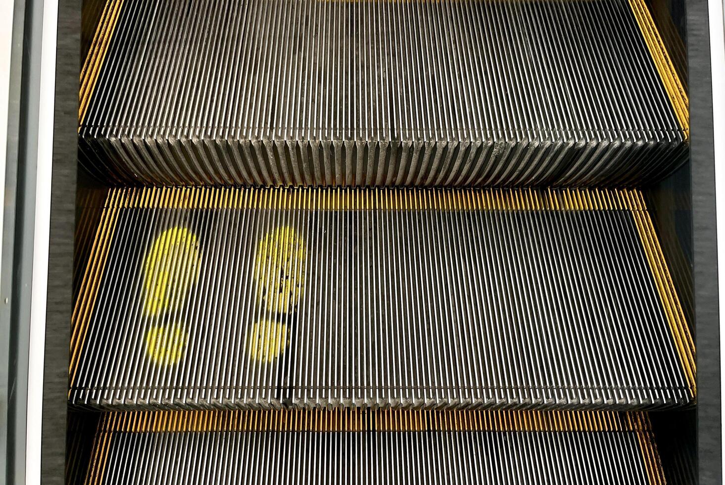 Old slightly faded yellow foot prints painted on escalator staircase with brushes on the left and right sides isolated on horizontal ratio background. photo