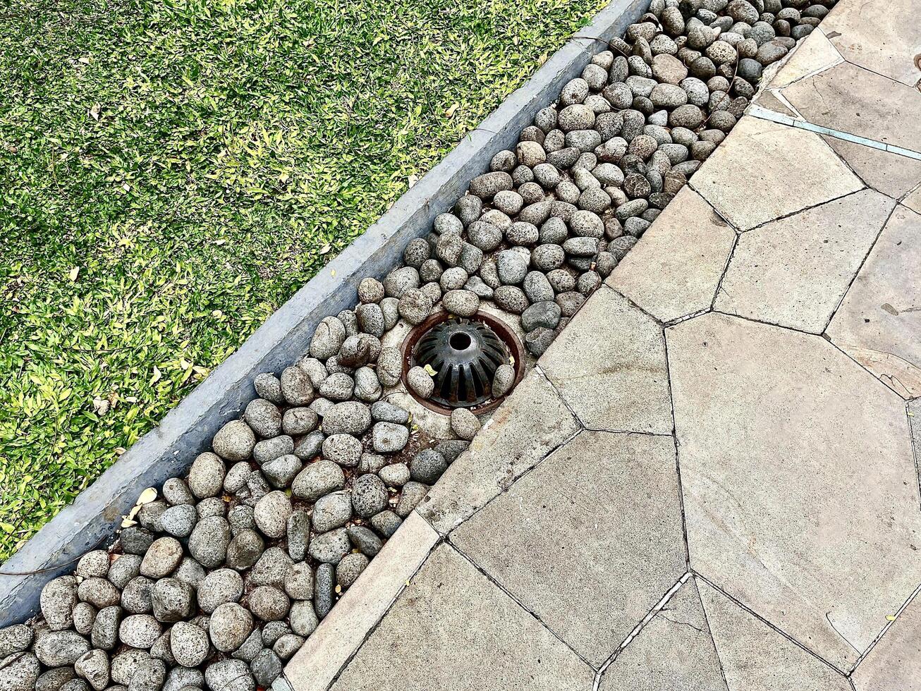 Park pavement ground stone flooring with green grass and metal iron drainage water hole isolated on horizontal ratio outdoor environment background. photo