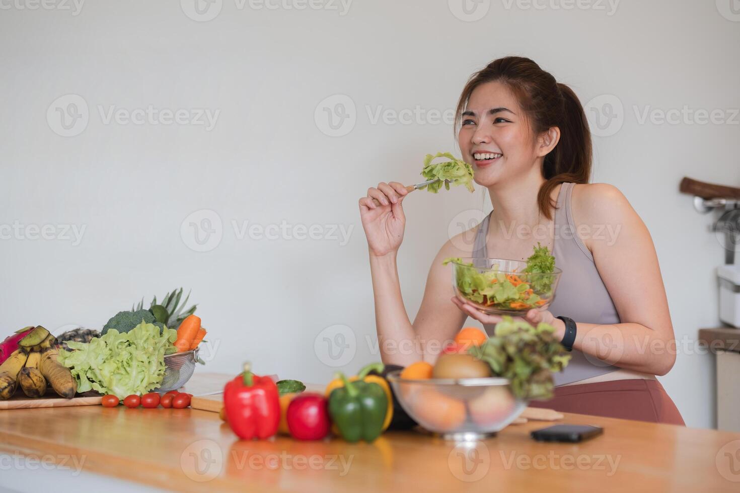 A woman is eating a salad in front of a table full of fruits and vegetables photo