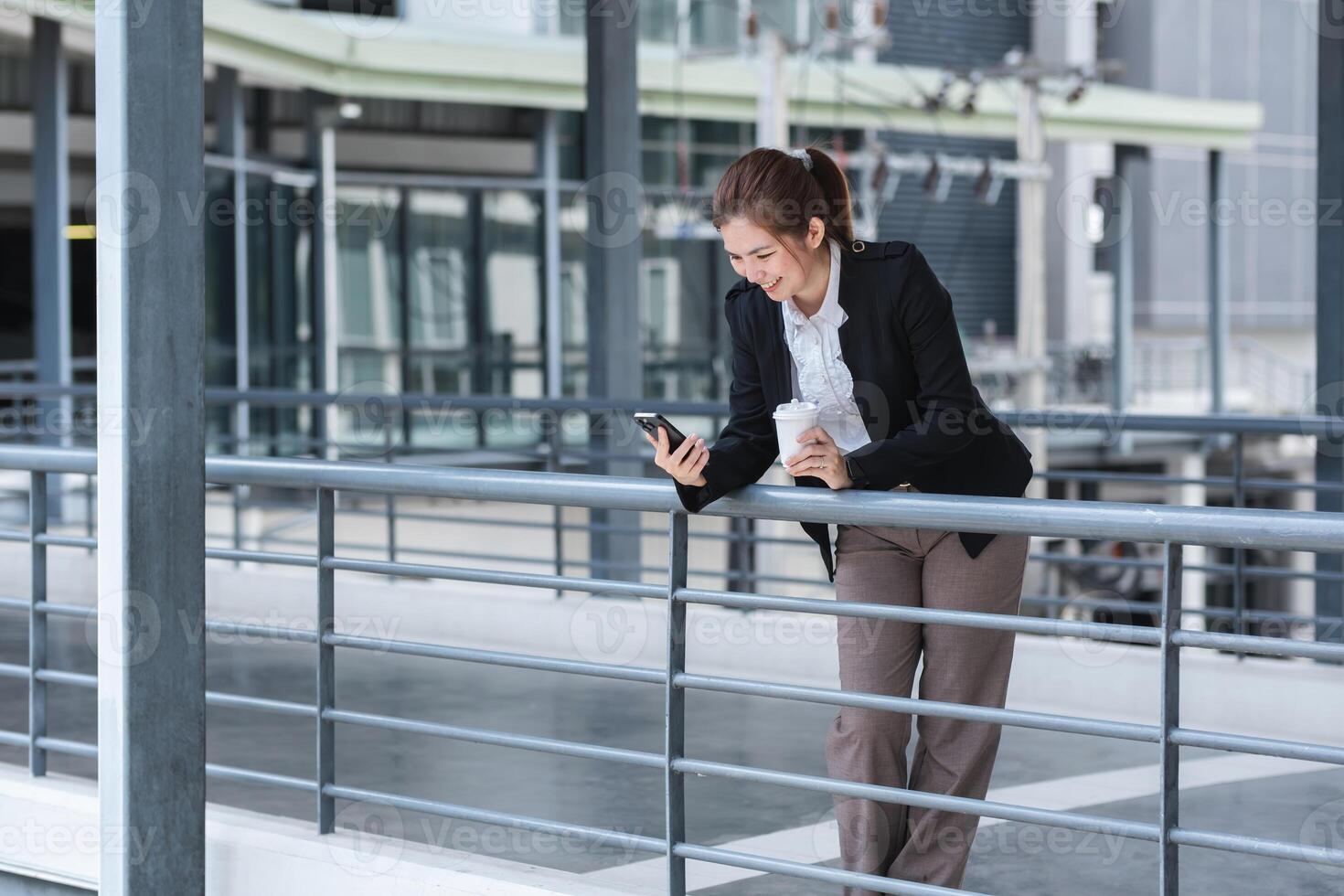 Asian businesswoman drinks coffee and discusses work on the phone in the hallway outside the office. photo
