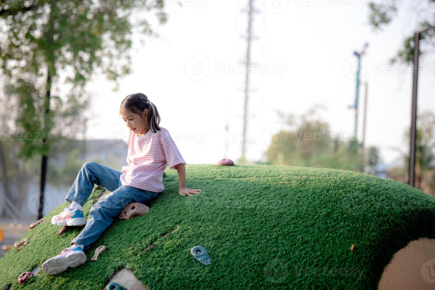 A little girl is sitting on a grassy hill in a park photo