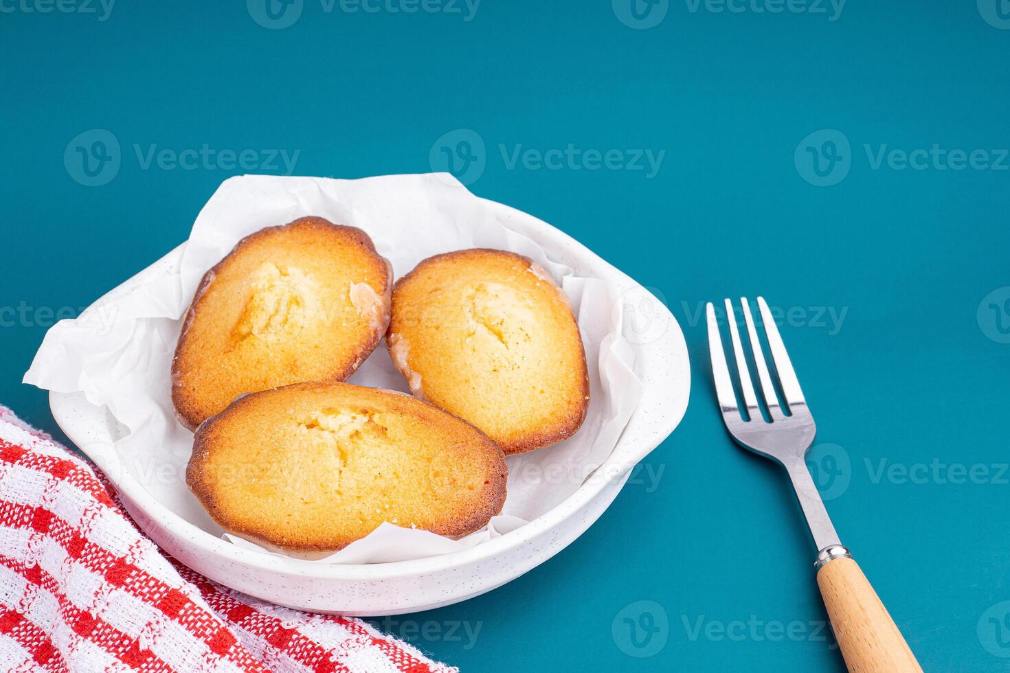 Lemon glaze madeleines on a plate placed on a blue light background. Madeleine - homemade traditional French small cookie. Seashell sweet cakes photo
