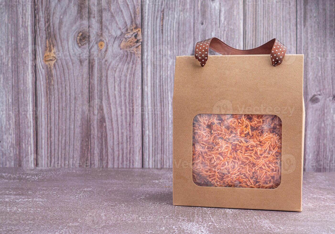 Package for sale of sweet and sour crispy noodles or Mee krob in the Thai language placed on a gray stone background. Side view with copy space for text photo