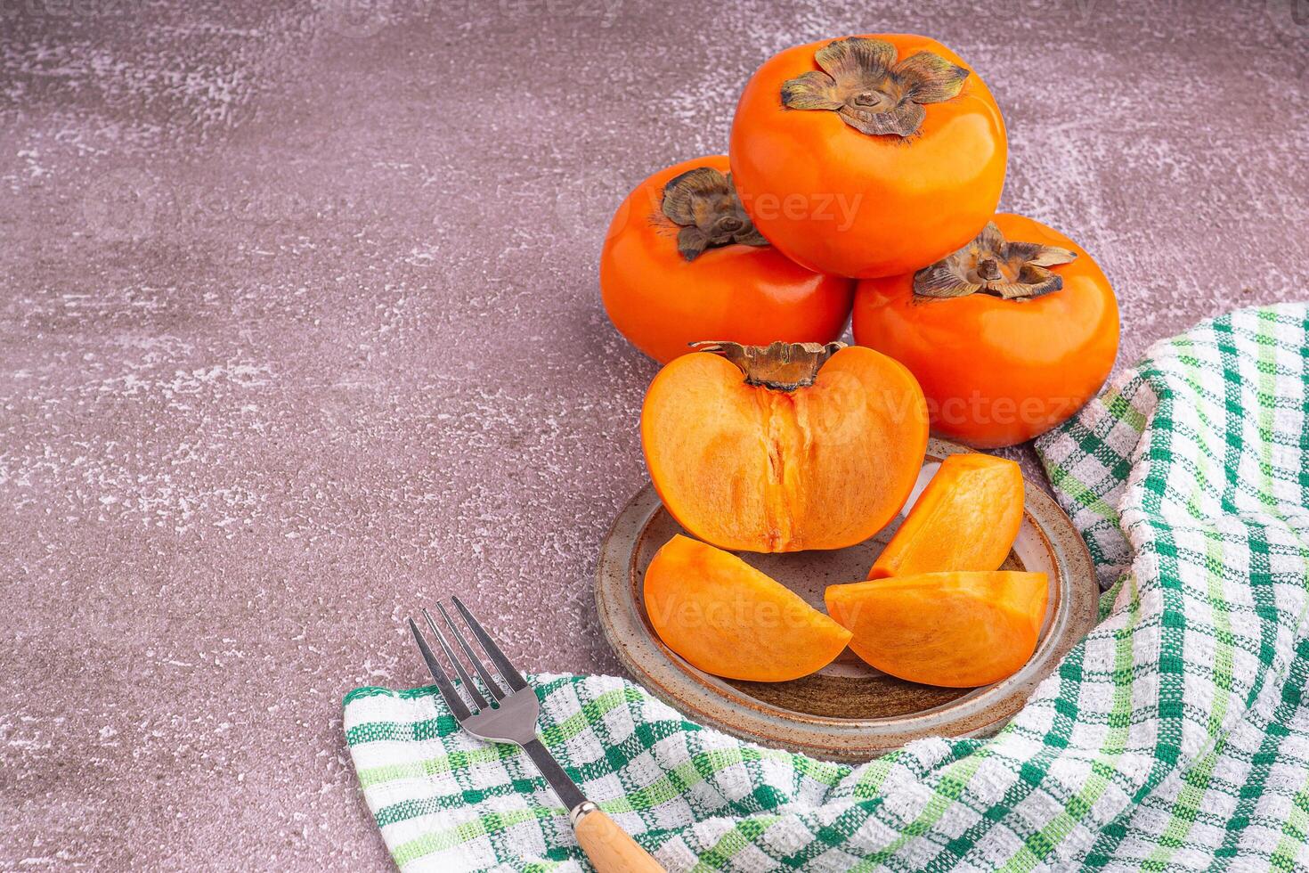 Fresh ripe persimmons with slices of persimmon on a plate with cutlery and whole fruit on gray stone background. Space for text. Close-up photo. Concept of health fruit photo
