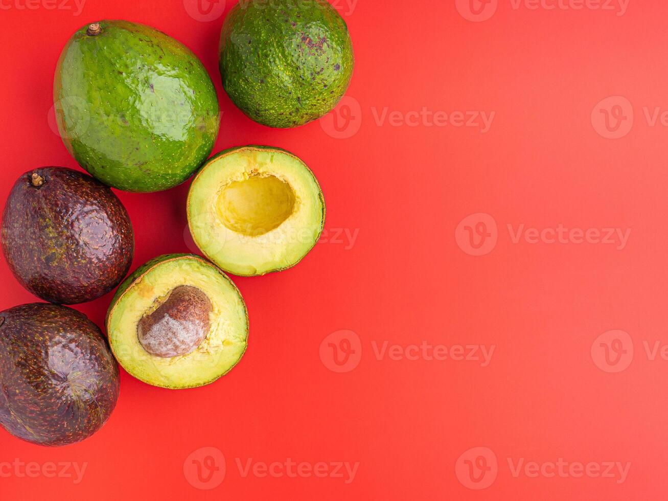 Organic avocado with seed, avocado halves and whole fruits on red background. Top view. Green avocados pattern in minimal flat lay style. Space for text. Concept of healthy fruit photo