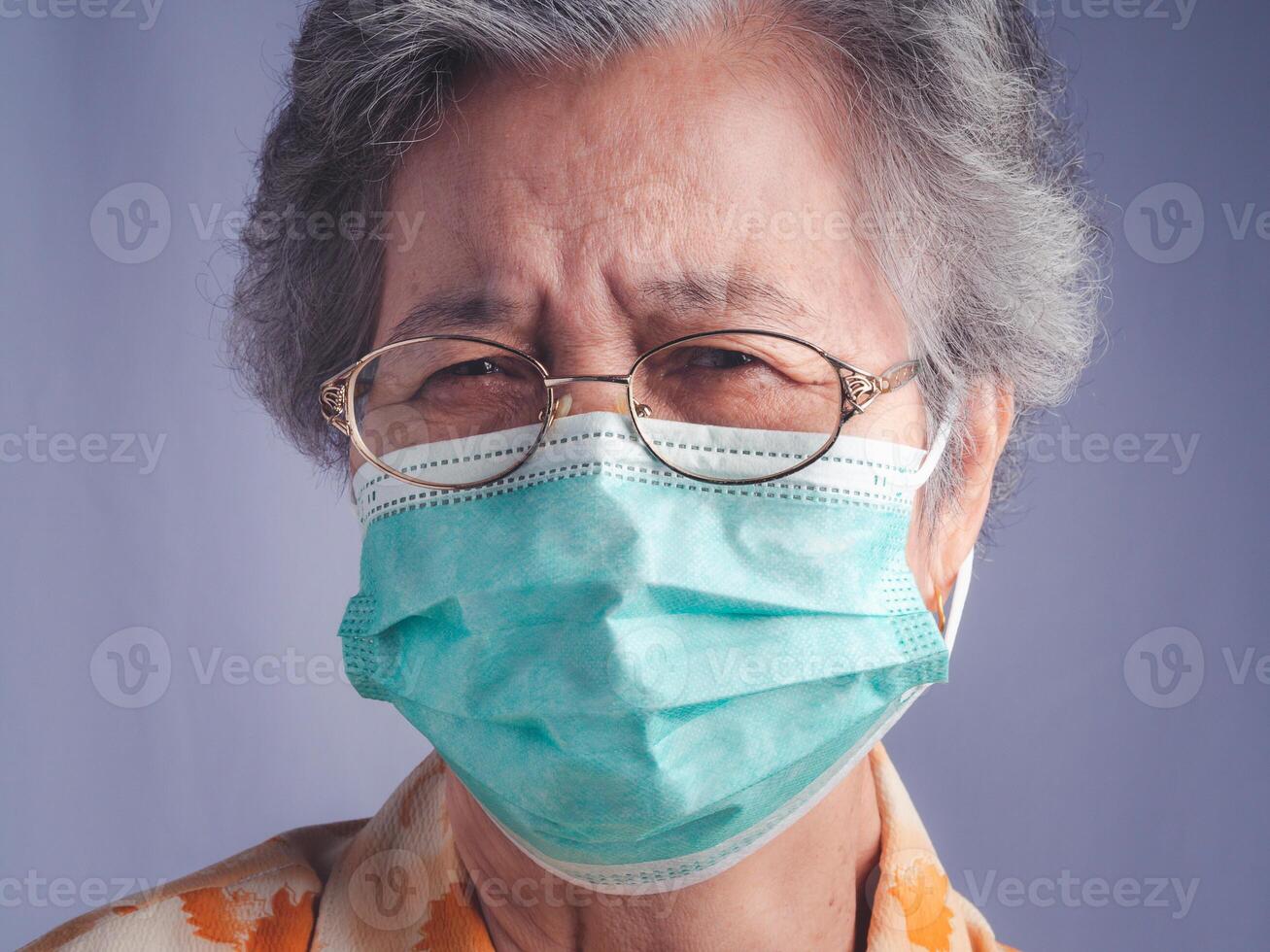Portrait of a senior woman with white hair wearing a mask and looking at the camera while standing with a gray background. Space for text. Concept of aged people and healthcare photo