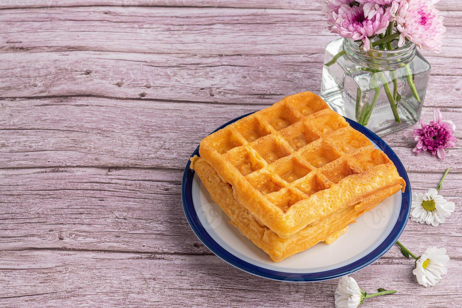 The waffle or Honeycomb dessert is placed on a white plate with flowers on a wooden table. Top view with space for text. Concept of dessert and relaxation photo