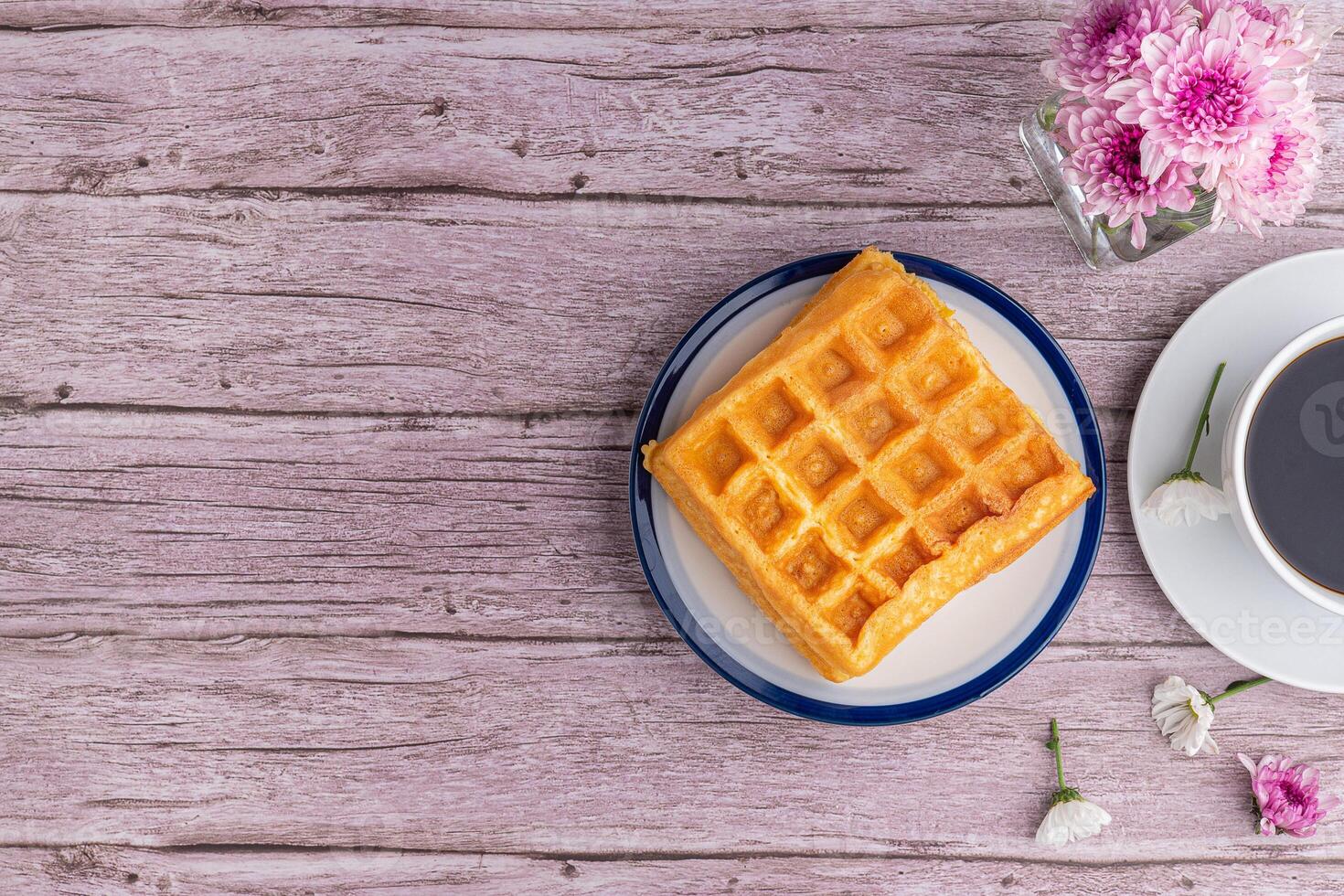 The waffle or Honeycomb dessert is placed on a white plate and a white cup of coffee with flowers on a wooden table. Top view with space for text. Concept of dessert and relaxation photo