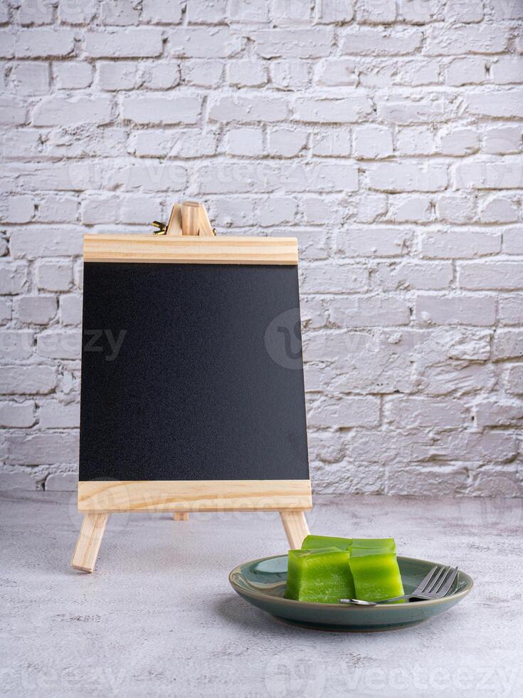Blackboard and layer sweet cake on a plate on gray stone background with white brick wall photo