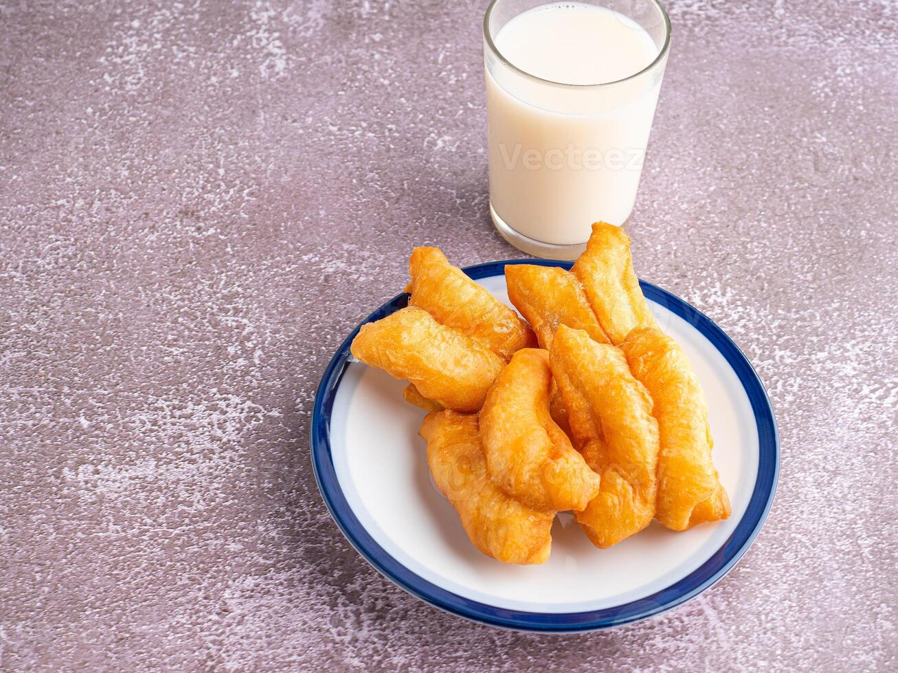 Top view of deep-fried dough sticks or Chinese doughnut sticks on a white plate and a glass of soybean milk on gray stone background. Space for text photo
