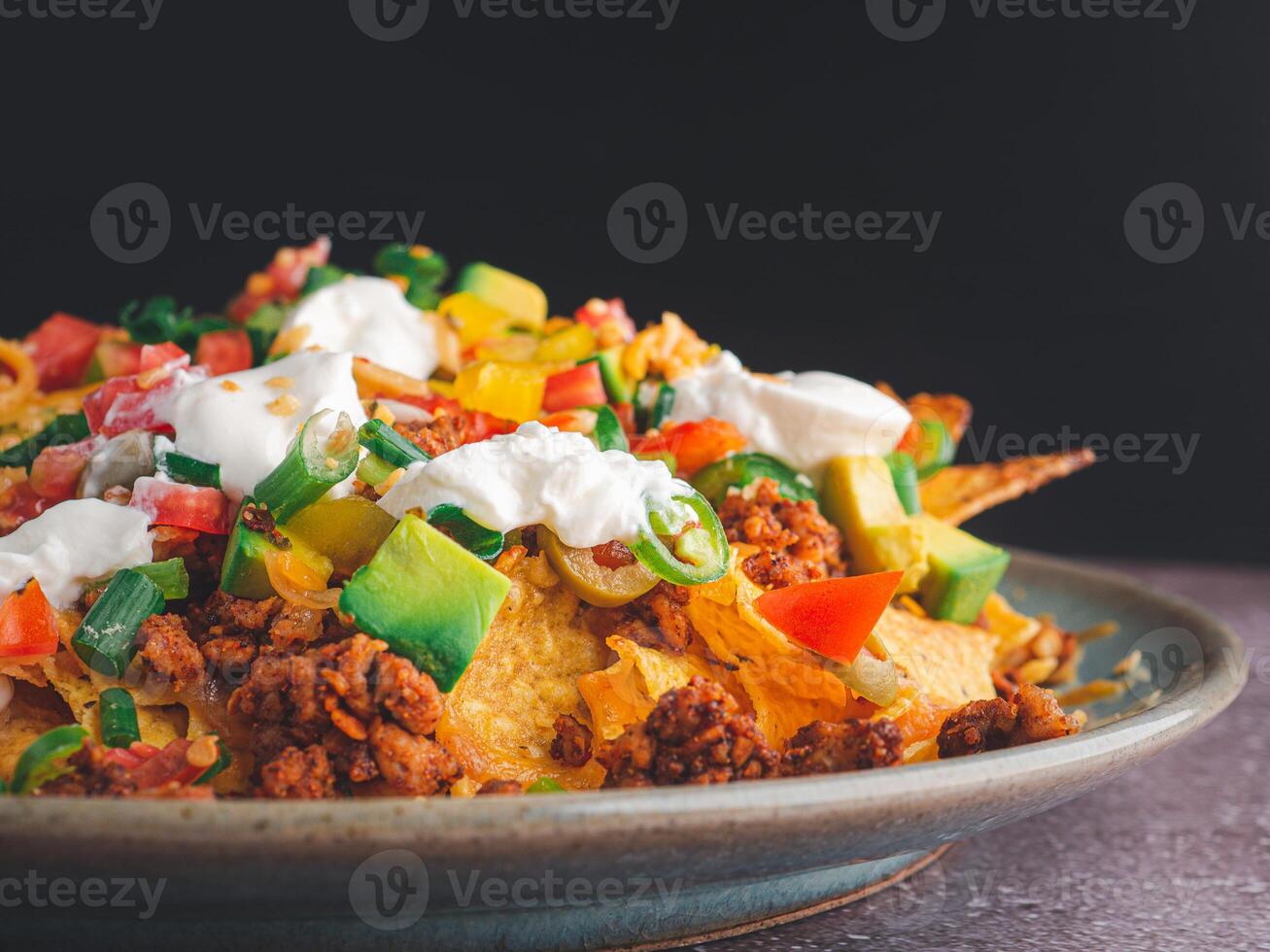 Side view of loaded minced pork nachos on plate with black wall background photo