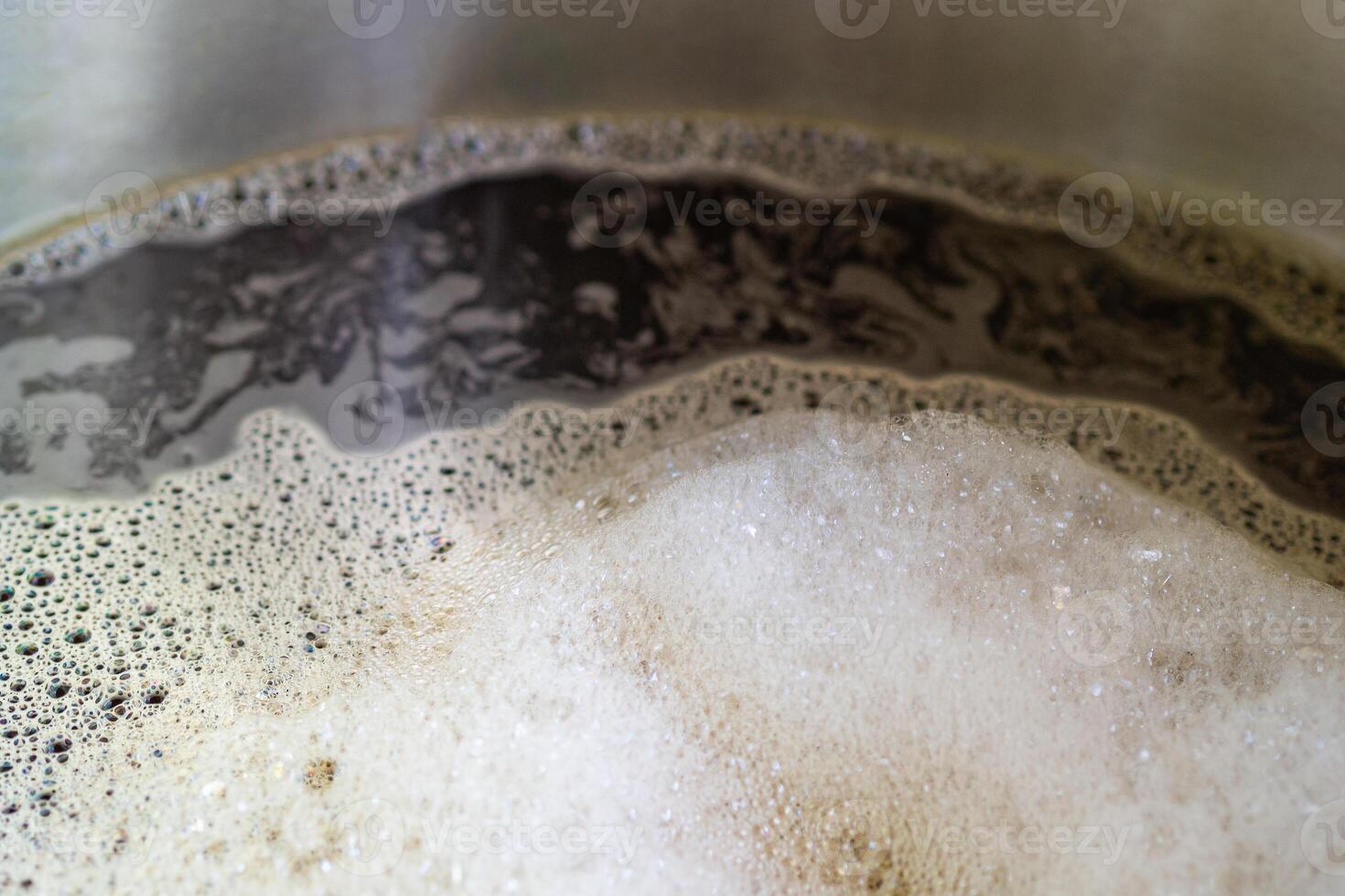 Close-up of craft beer and foam in a fermentation container. Process of making home beer from malt. Craft beer from barley and dark malt. Selective focus photo