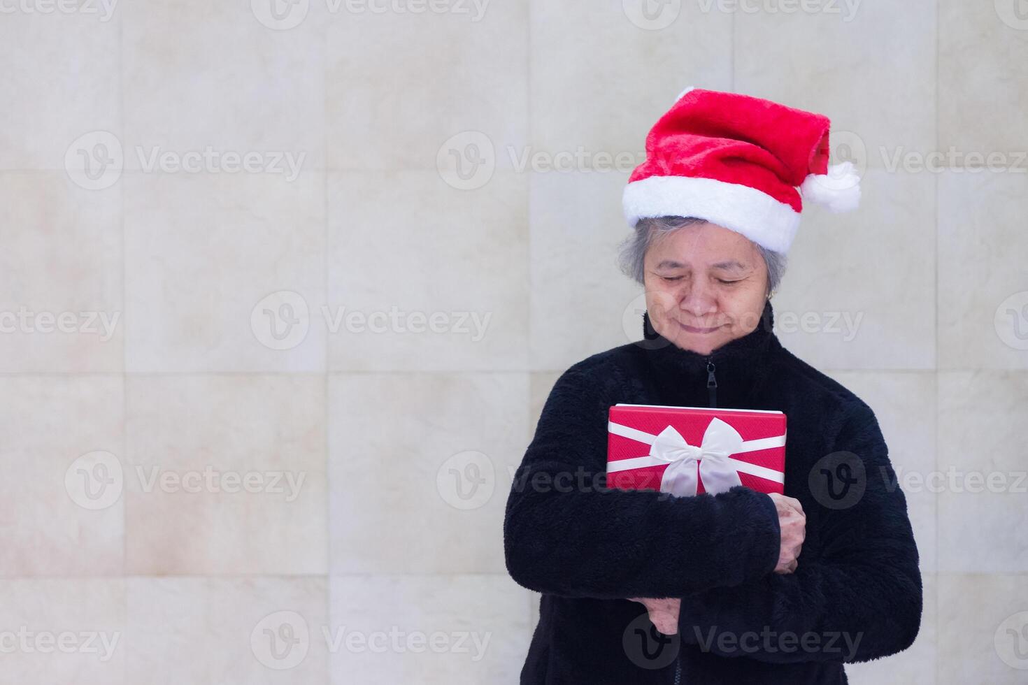Portrait of a senior woman hug and looking at a gift box while standing in the home photo