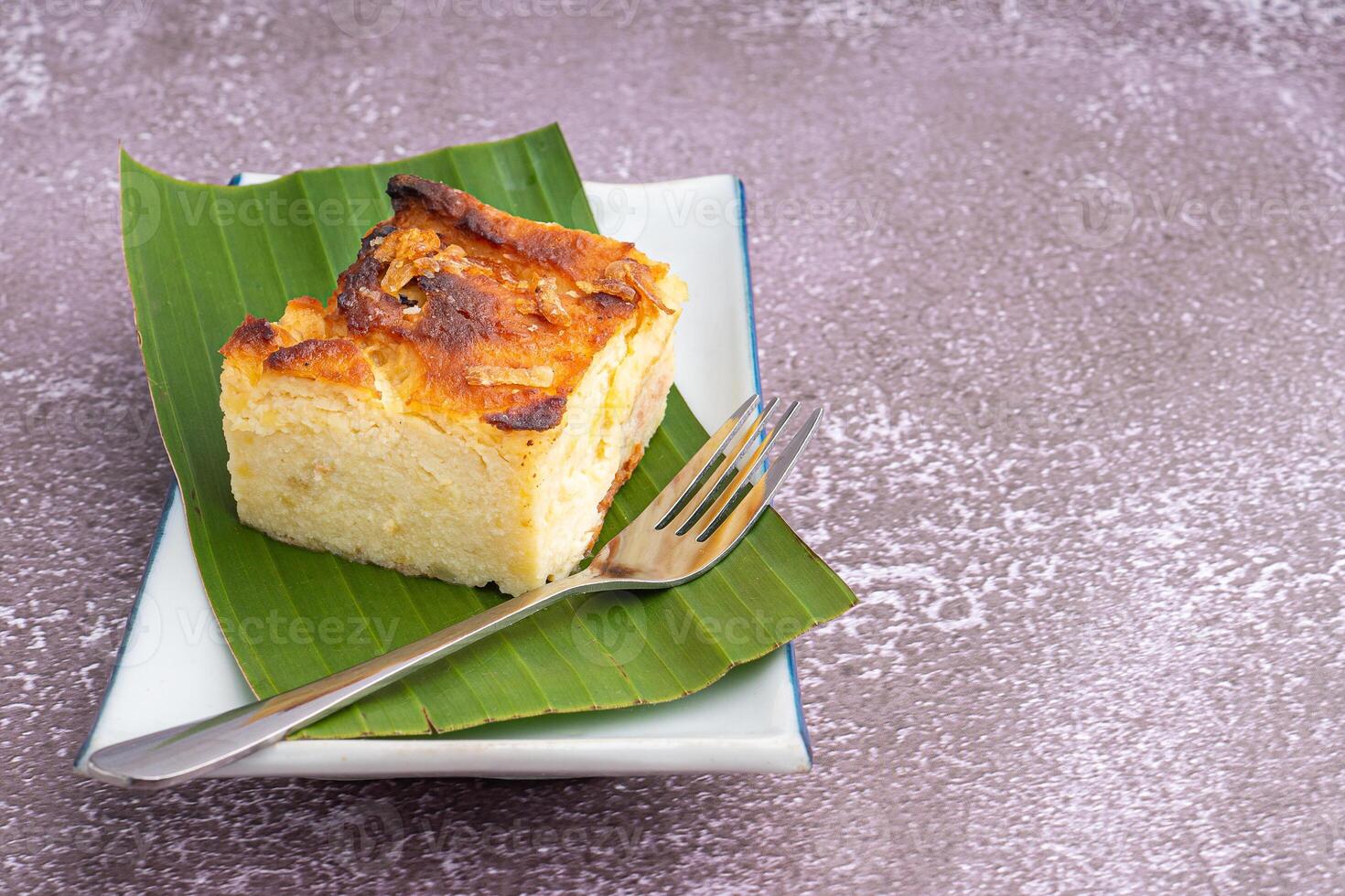 Thai custard cake on banana leaf and spoon on a white plate with a stone background. Egg custard with mung bean flour. Thai dessert is famous. Space for text photo