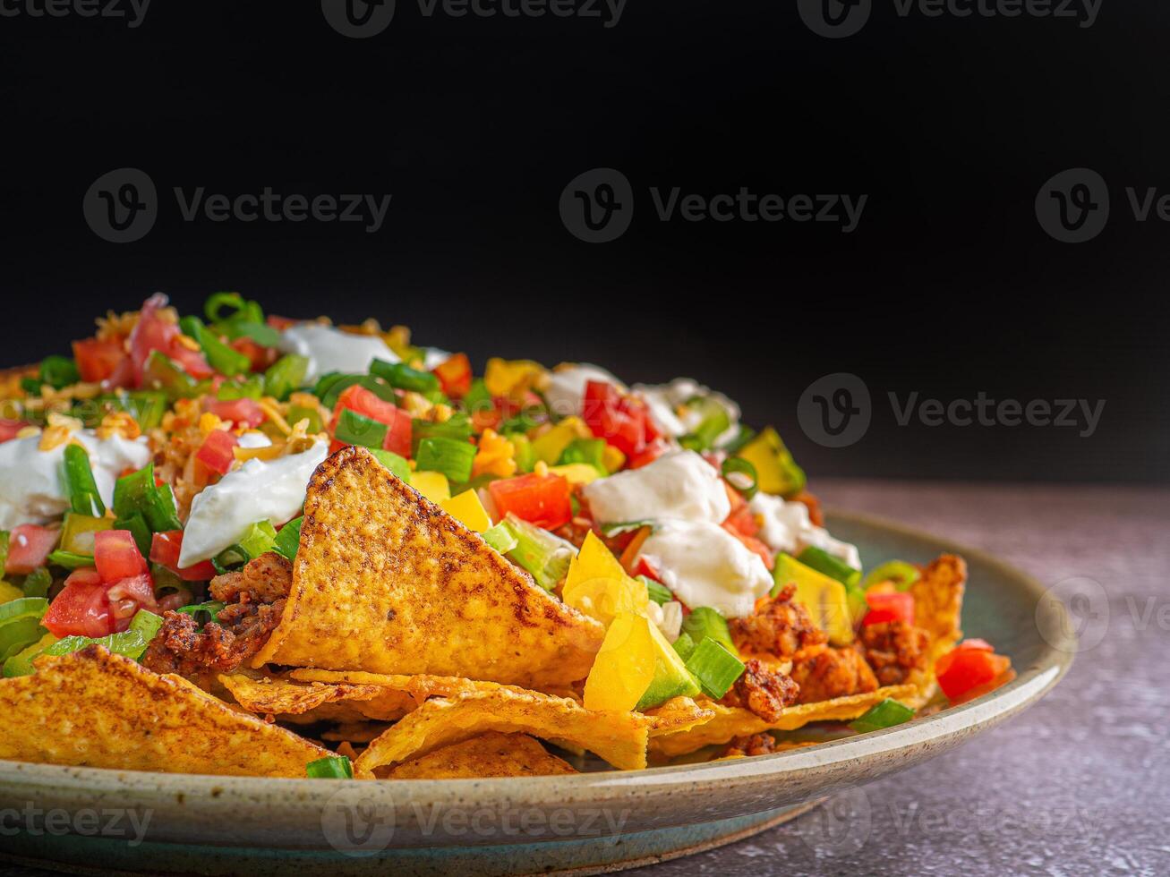 Side view of loaded minced pork nachos on plate with black wall background photo