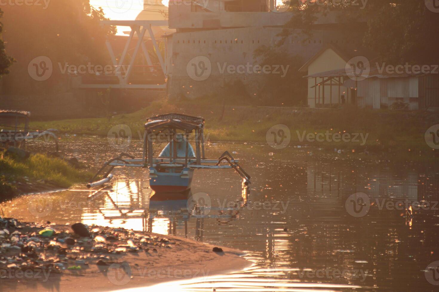A traditional boat moored in a polluted river near riverside buildings in the serene morning light with golden sunlight, creating a tranquil atmosphere. photo