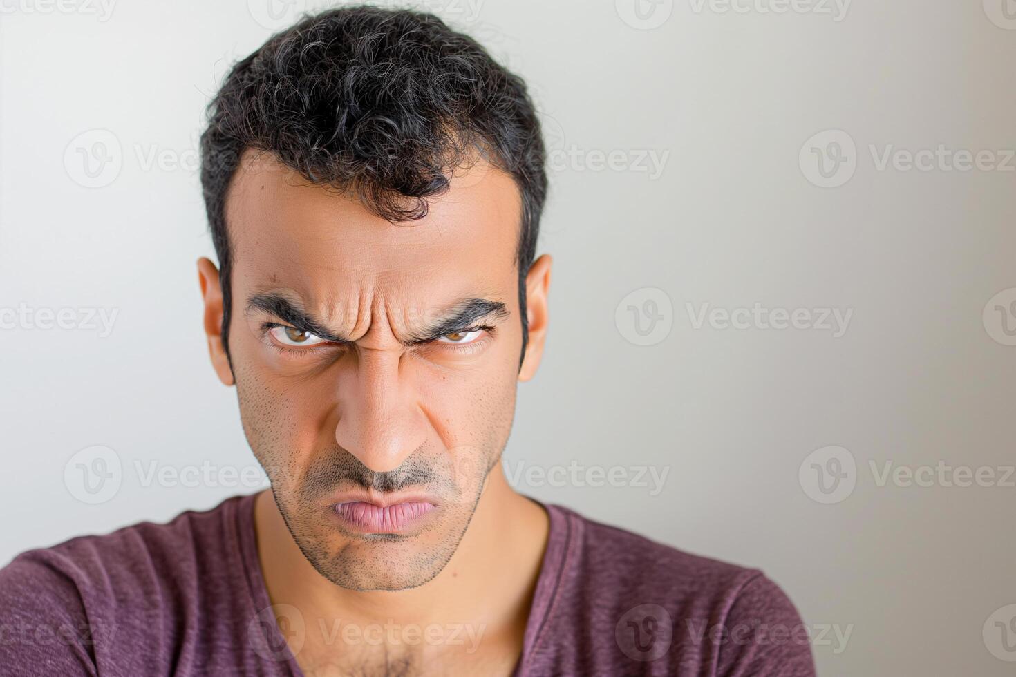 Angry Young Middle Eastern Man in Maroon Shirt with Intense Expression on Light Background photo