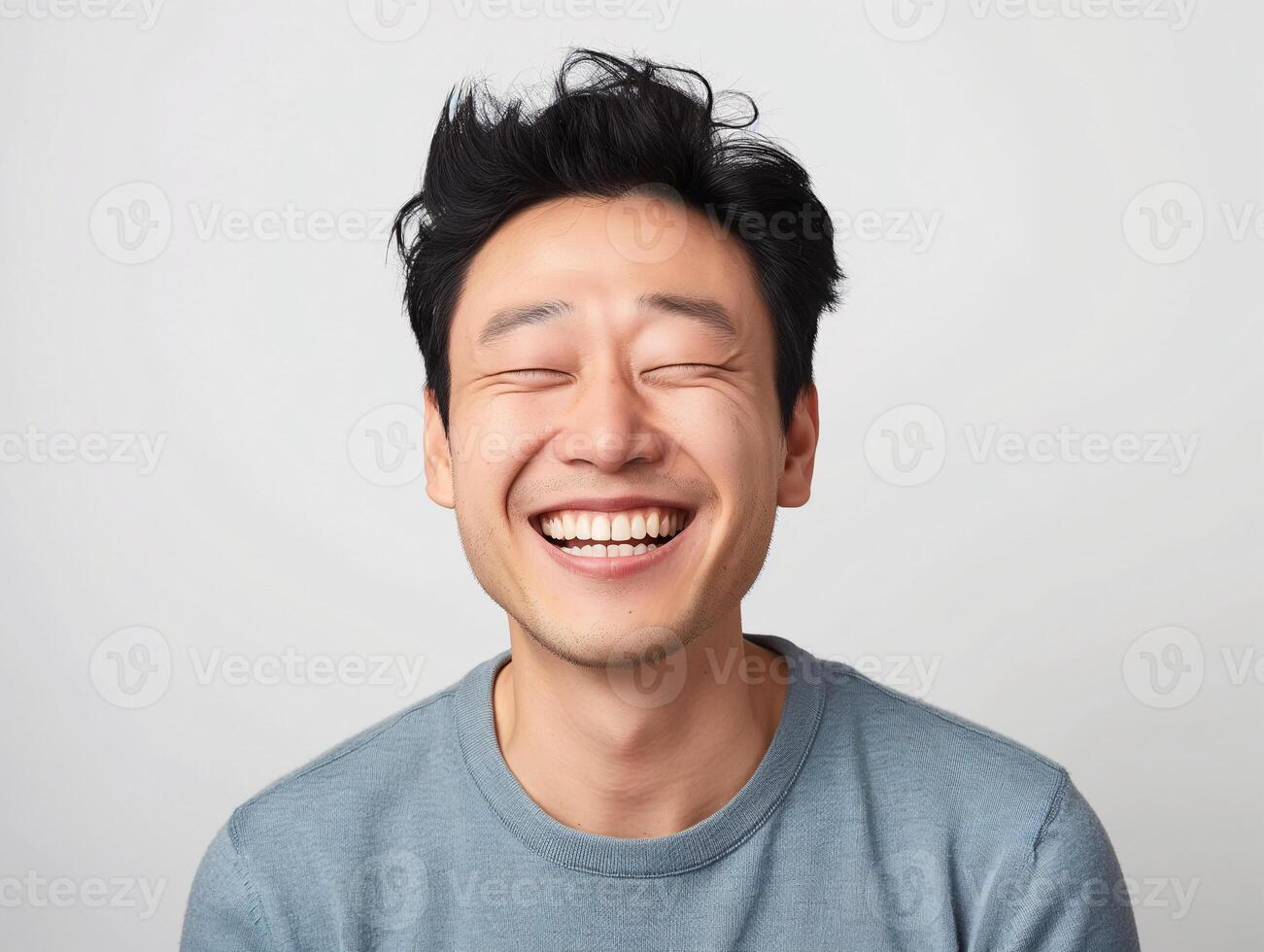 Happy Young Asian Man Smiling with Eyes Closed in a Casual Blue Sweater on a White Background, Expressing Joy and Contentment photo
