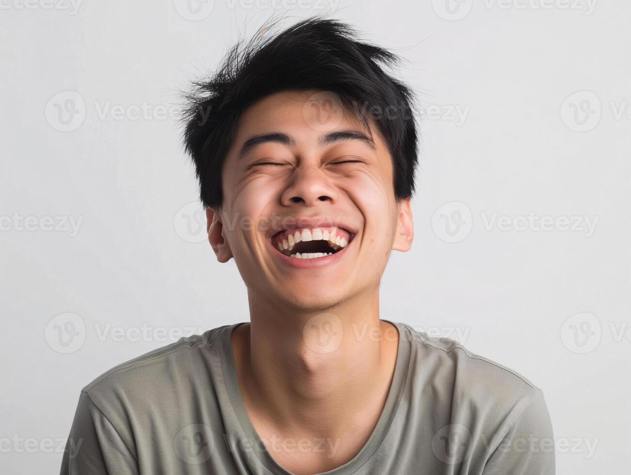 Young Asian Man with Closed Eyes Laughing Heartily, Expressing Joy and Happiness on Plain Background photo