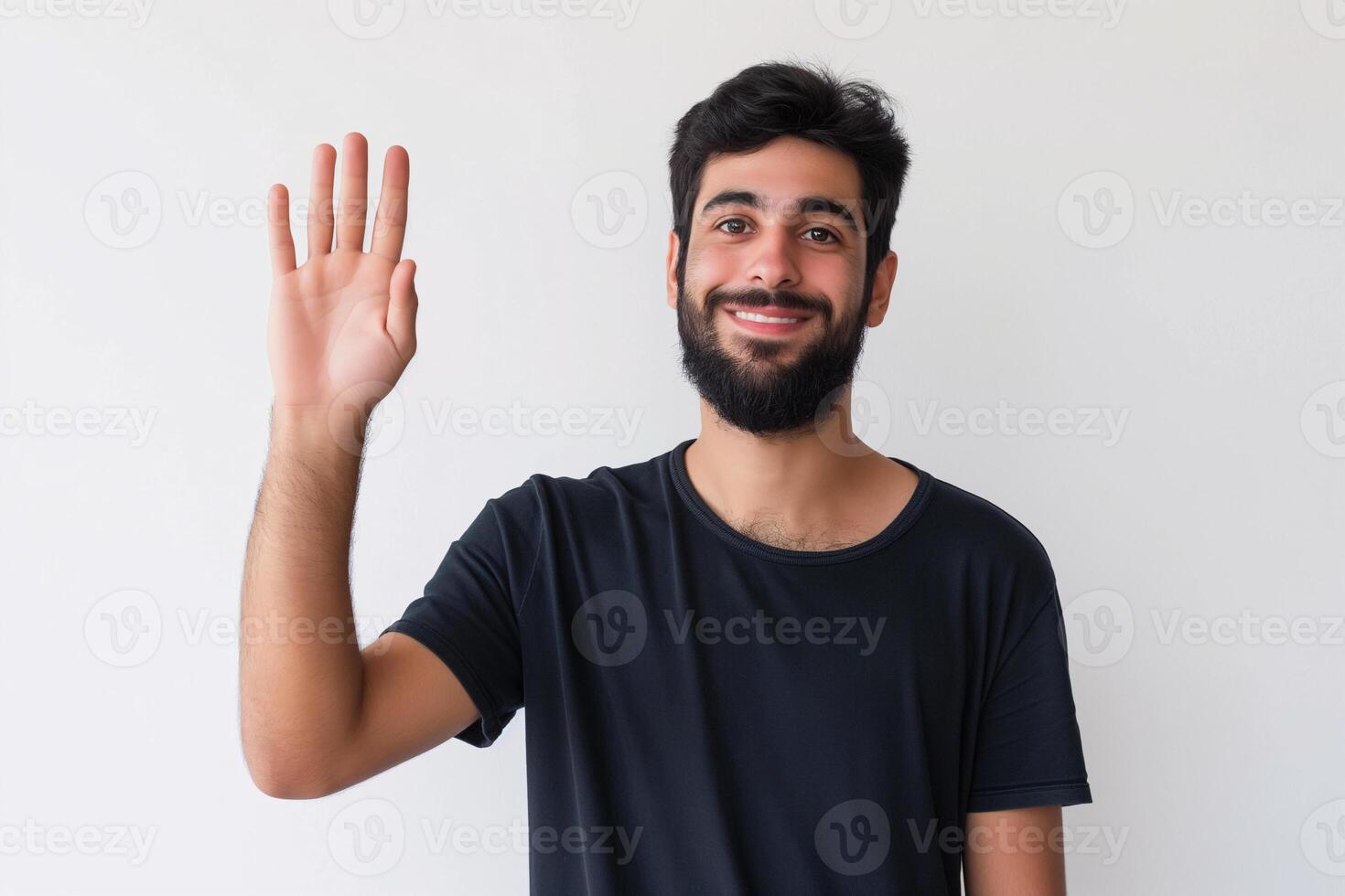 Friendly Young Man with Beard Wearing Black T-Shirt Waving Hello in Studio Portrait on White Background photo