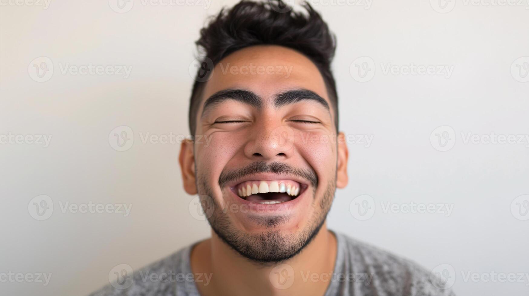 Close-up Portrait of a Young Man Laughing with Eyes Closed, Expressing Joy and Happiness in a Casual Gray T-shirt Indoors photo