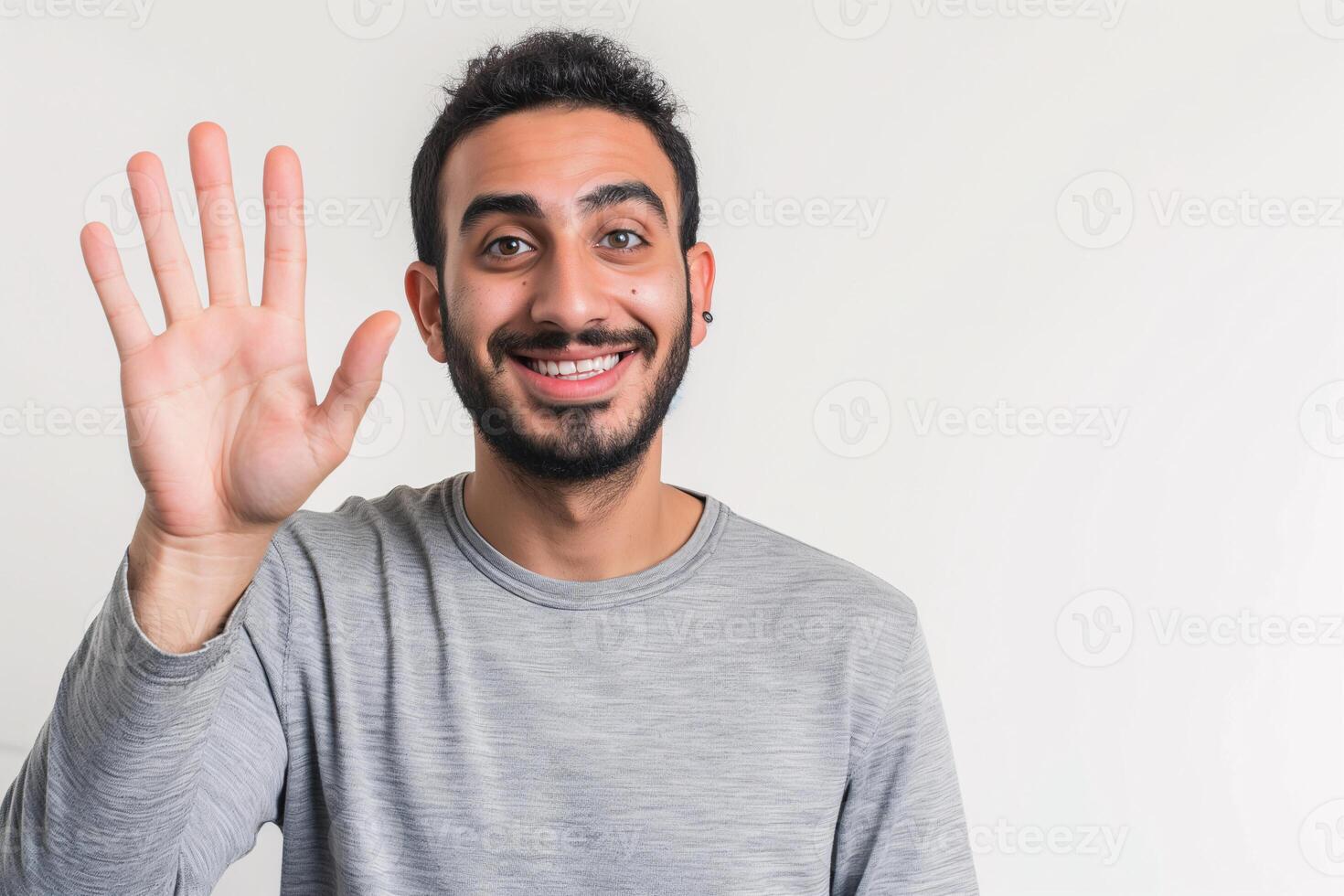Cheerful Middle Eastern Man in Grey Shirt Waving Hello with a Friendly Smile photo