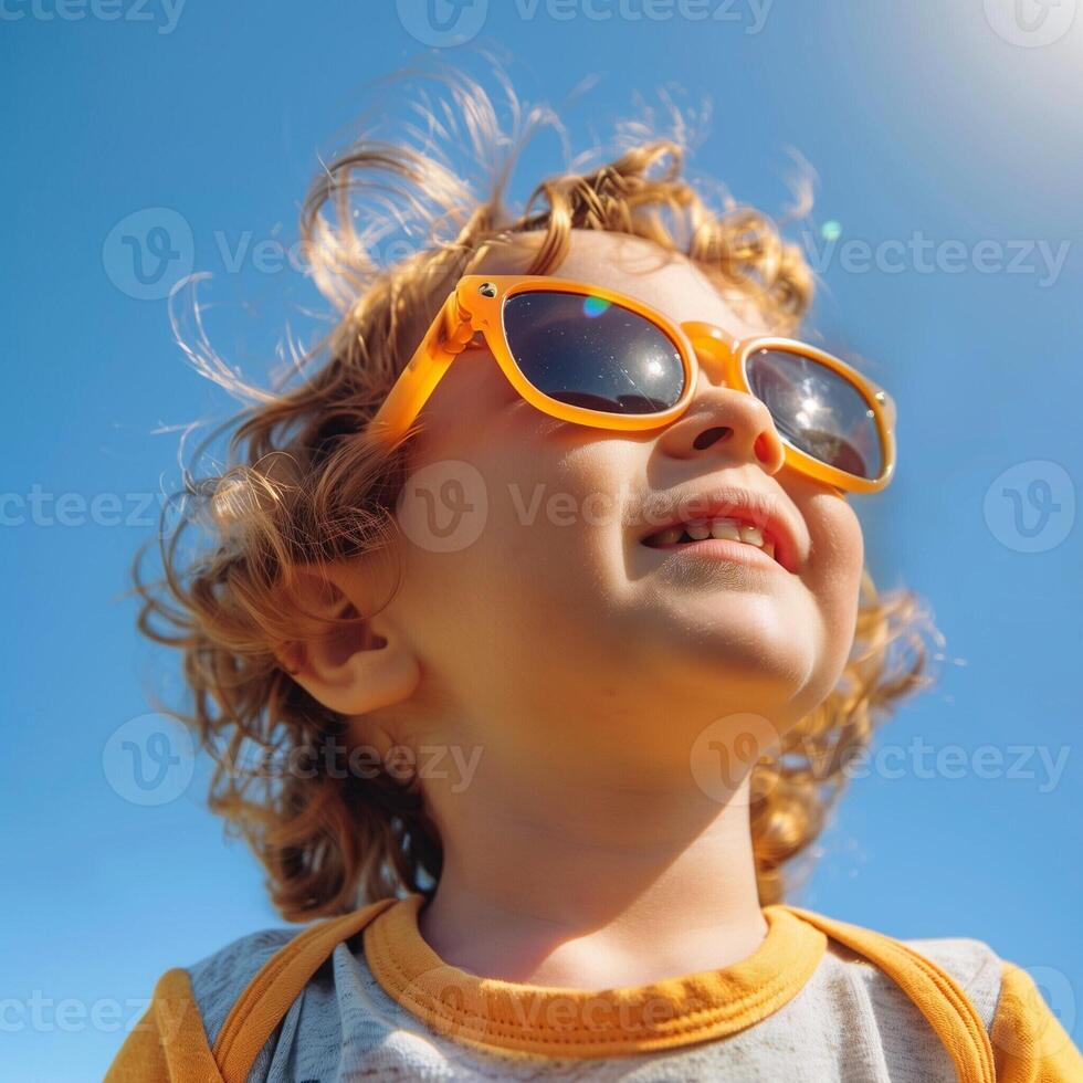 Cute little child in sunglasses smiles and looks at the bright sun and sky. Children concept. photo