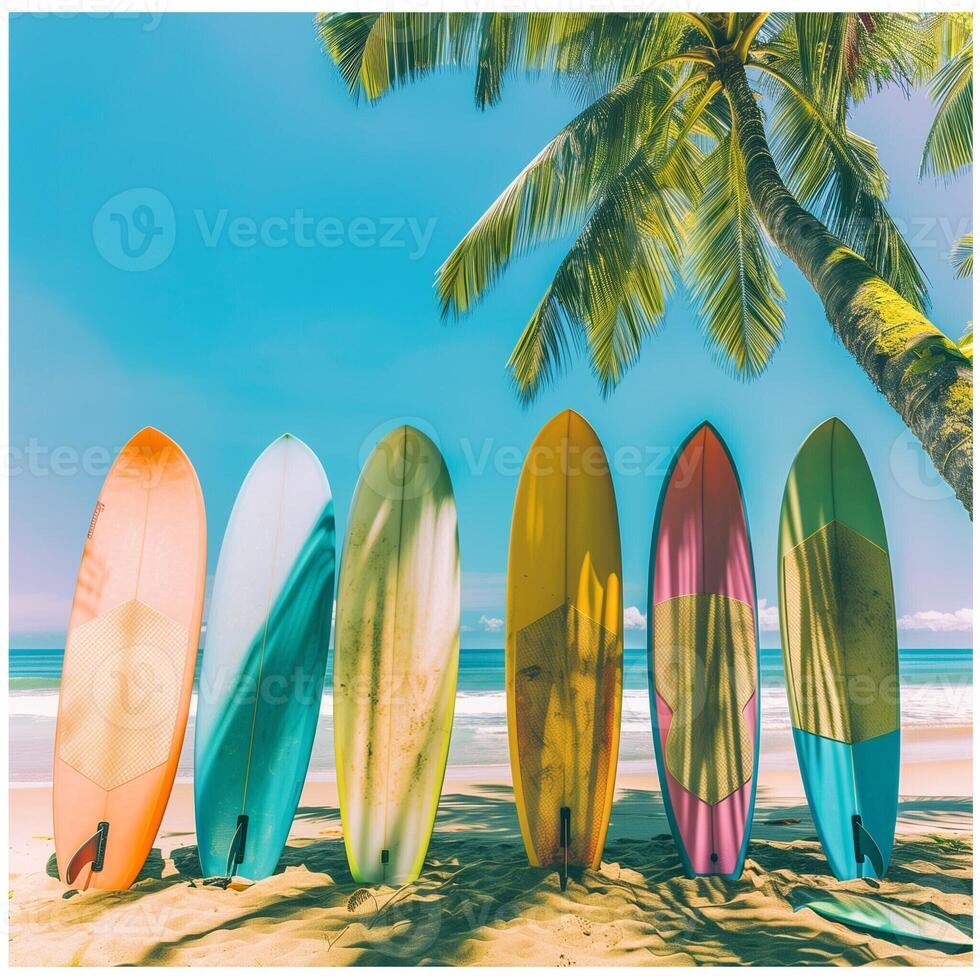 A collection of colorful surfboards lined up on a white sandy tropical beach surrounded by palm trees and the turquoise ocean in the background. photo